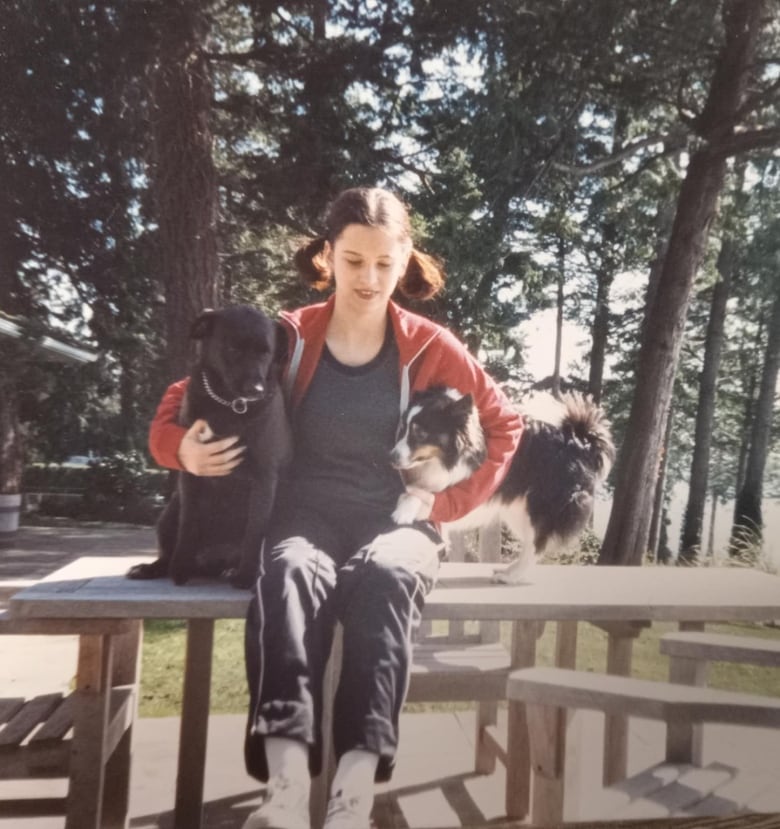 A girl sits on a bench with two small dogs. 