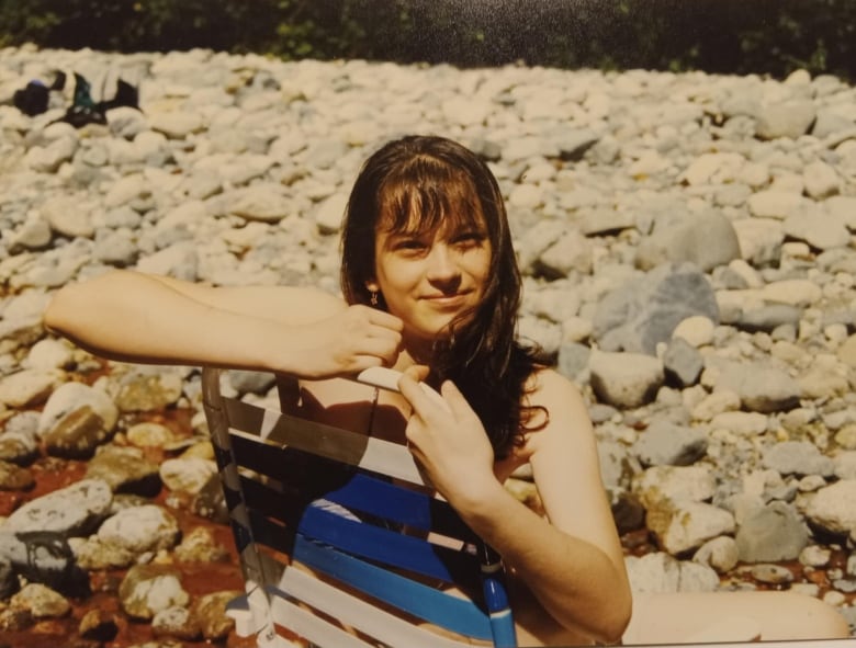 A girl sits on a chair in front of stones. 