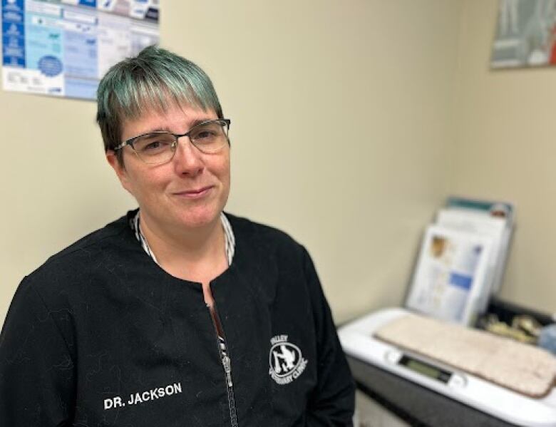 Woman with short blue hair smiles wearing black smock