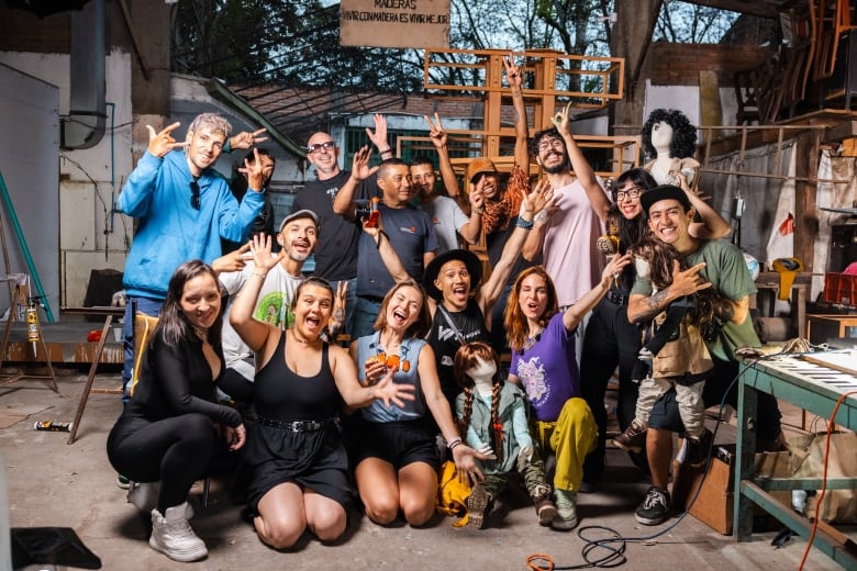 A group of smiling people pose together in an art studio. Some flash sighs with their hands. Some are holding sculptures of people and animals.