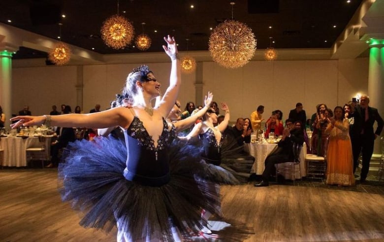 Dancers wearing purple dresses performing at a gala, with spectators siting behind them 