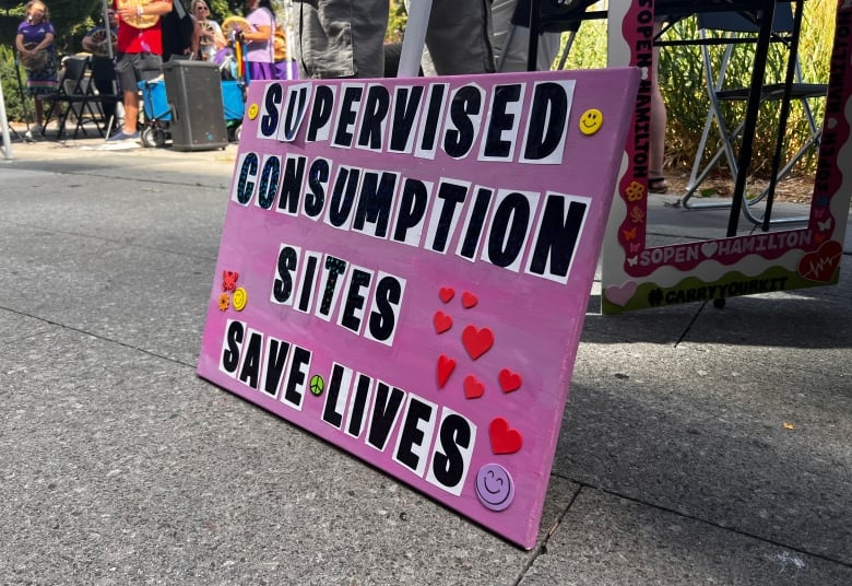 A pink sign that reads 'Supervised Consumption Sites Save Lives.'