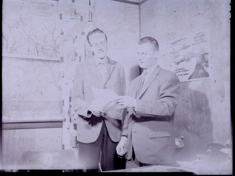 A black and white photo of two men looking at a piece of paper