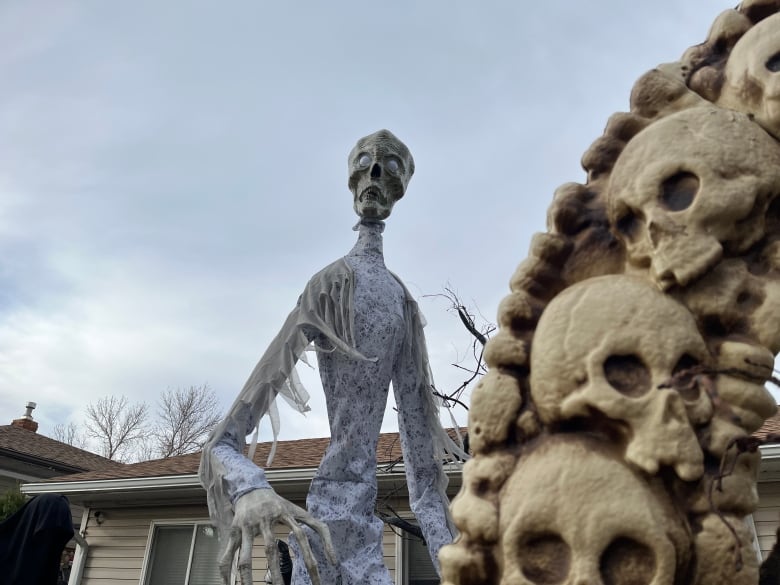 A large white skeleton stands in front of a grey sky at a haunted house. 