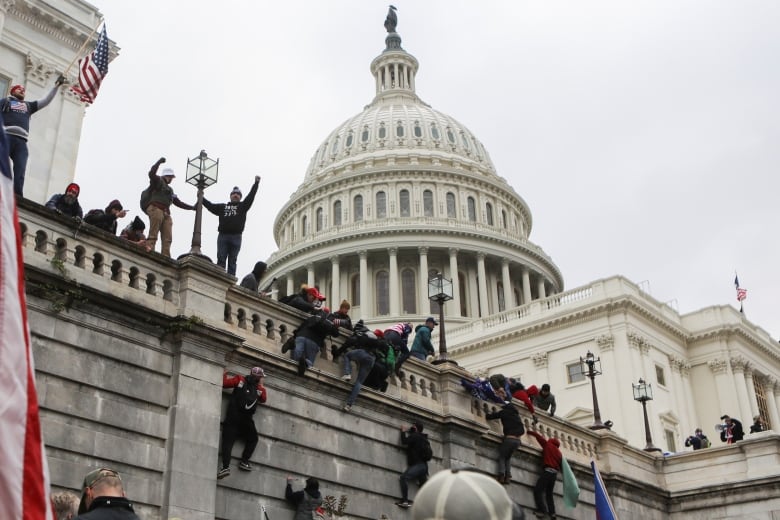 People scaling the wall of the US Capitol, beneath the dome