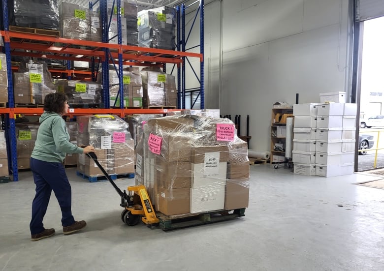 A person pushing a large pallet with cardboard boxes on them is shown.