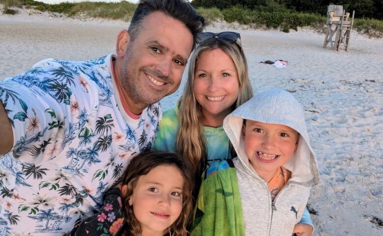 A father, mother and two children smiling for a selfie on a beach. 