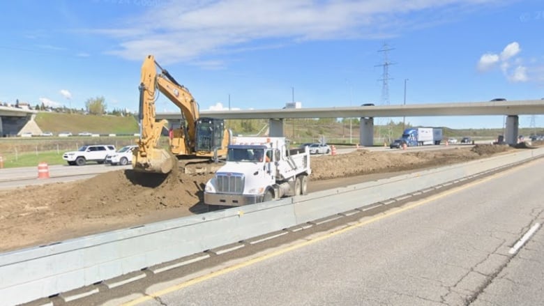 Construction trucks and equipment work between the road.