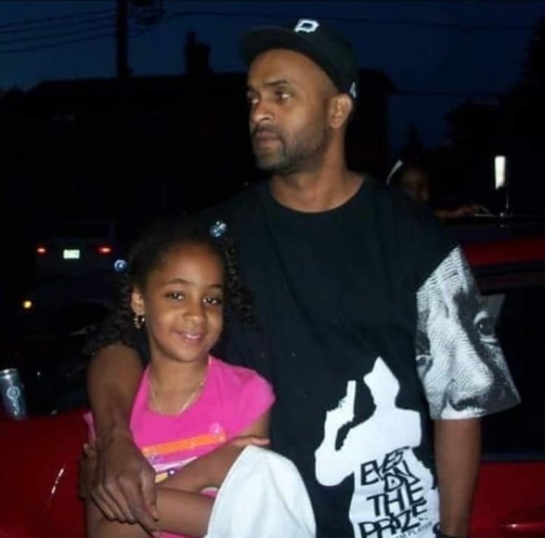 A young child in a pink shirt standing next to her father, who has his arm around her 