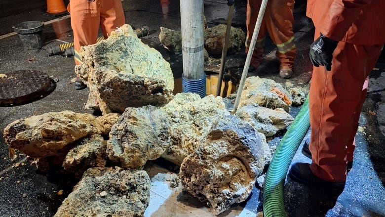 Workers stand looking at hardened fat deposits taken out of a sewer. 