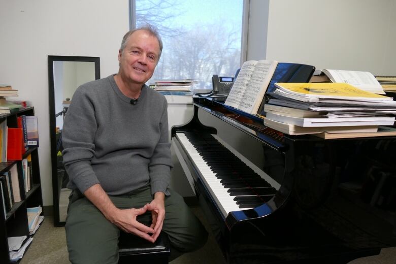 A man in a grey shirt sits at a piano.