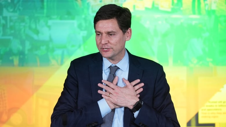 David Eby, a man in a suit, holds his hands over his chest.