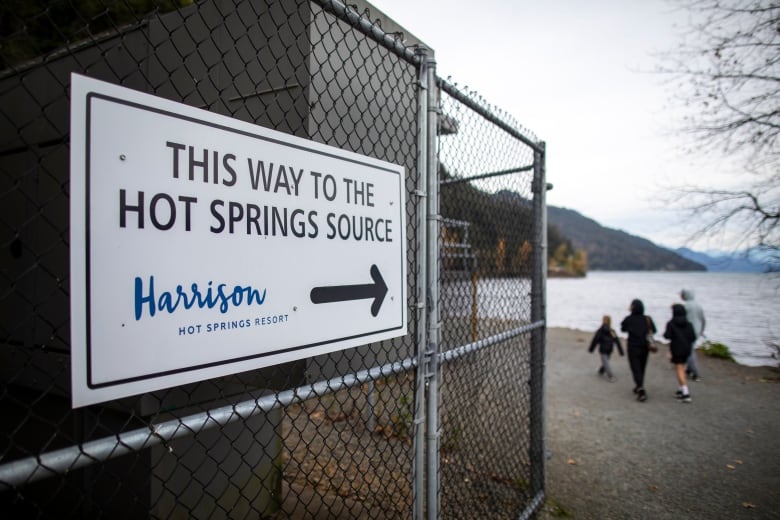 A sign pointing to the source of the hot springs as a family of four make their way to the source in the background. 