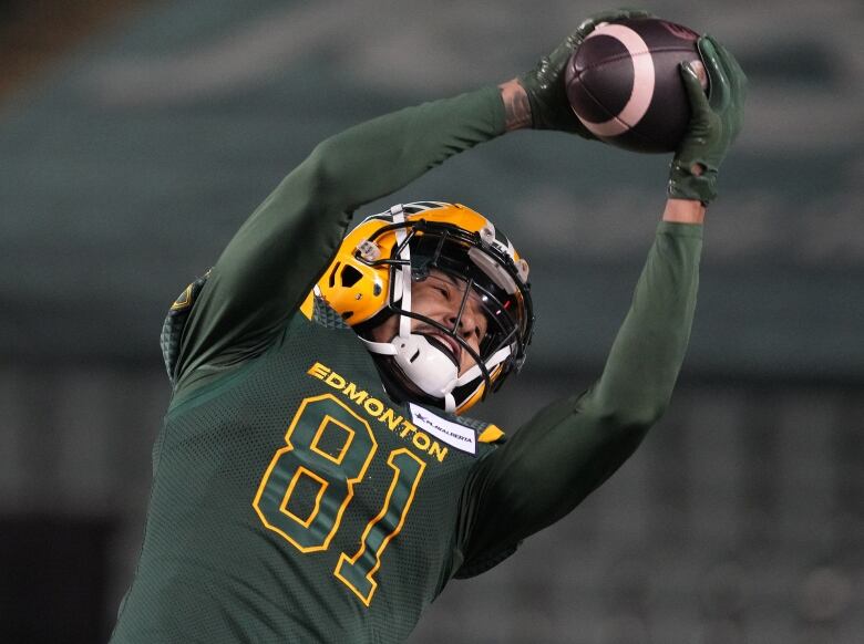 A football player in a green-and-yellow uniform stretches his body to catch a football.