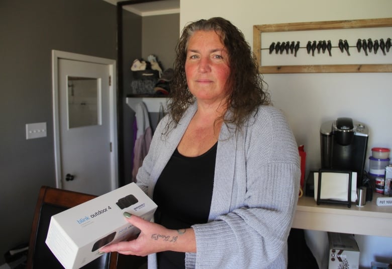 A woman in a grey sweater draped over a black dress stands while holding a white box