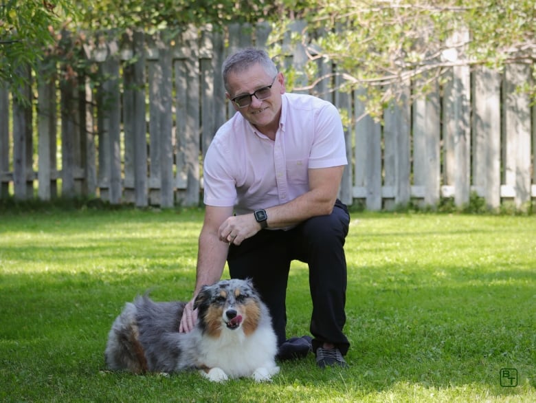 Man kneeling down on grass to be besides dog.