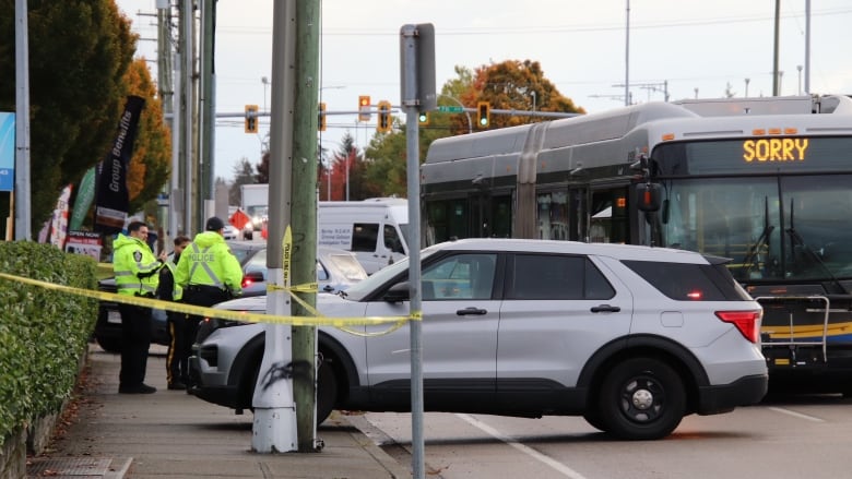 A scene of a collision with a yellow tape, a couple police officers in green reflective jackets a compact SUV and a transit bus. 