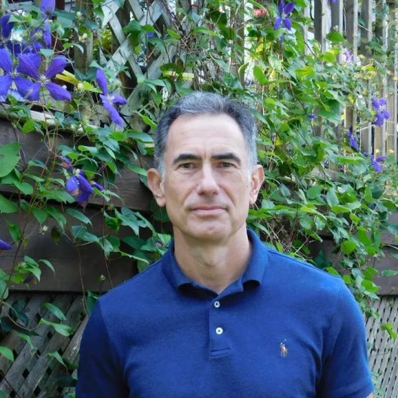 A man stands in front of a garden fence.