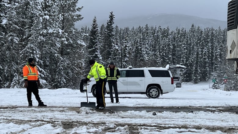 People n safety vests are seen shovelling snow off a road.