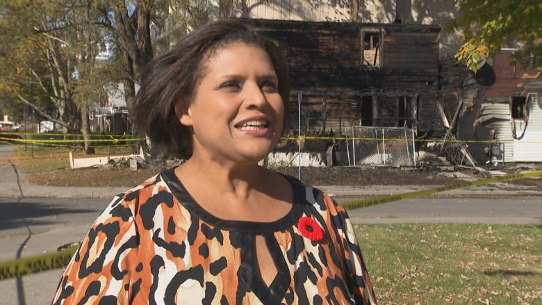 A woman stands in front of a burned house.