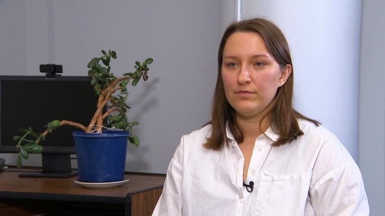 A woman in a white shirt looks at the camera