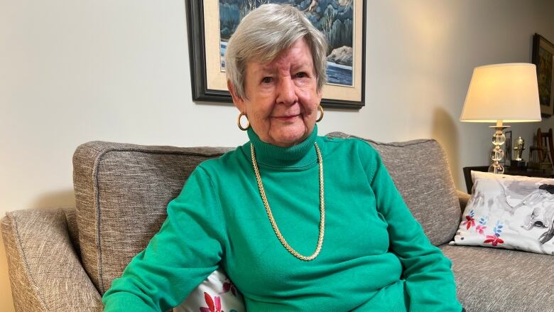 A woman with short, grey hair hair wearing a green sweater sits on a couch.