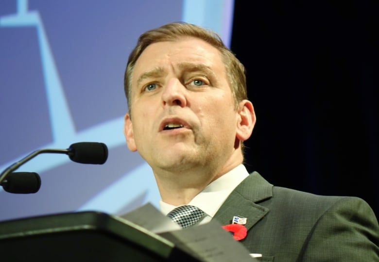 A man wearing a suit stands in front of a microphone at a podium.