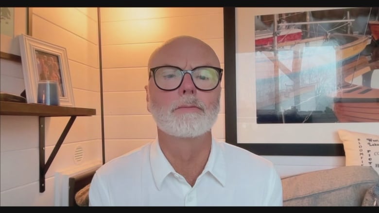 A man with a white beard and a white shirt sitting on a couch.