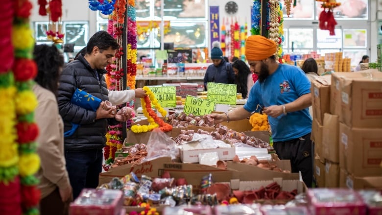 A number of people mill around near a shop display, with numerous signs celebrating Diwali.