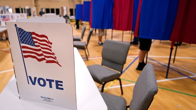 Interior of polling station, likely gymnasium. A voting privacy screen sits on a folding table. 