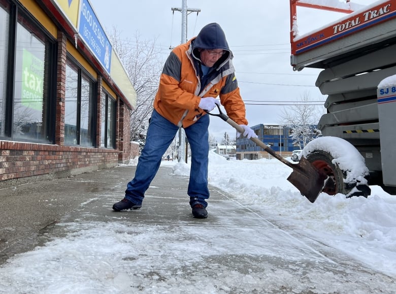 A man shovels snow off a sidewalk.