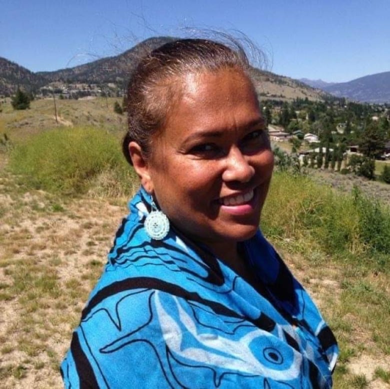 An Indigenous woman smiles while outdoors on a sunny day.