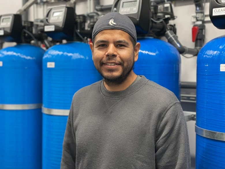 Smiling man in a grey shirt stands in front of blue filtration tanks.