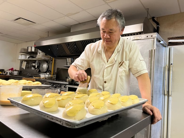 A man uses a pastry brush to paint a glistening sheen on golden buns.