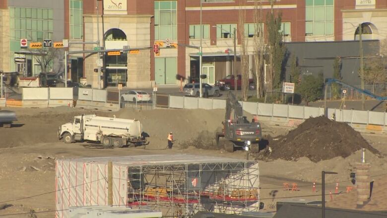 Construction equipment digs through large piles of dirt near an intersection.