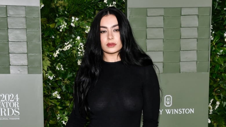 a woman with black hair in a black dress stands in front of a green backdrop to take pictures for an event