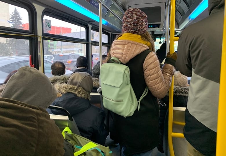 People are seen from the back, standing and sitting on a bus