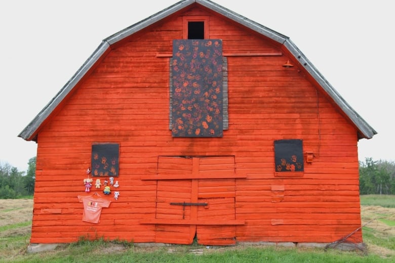 An orange barn with planks bearing handprints, as well as some toys hanging on its faade