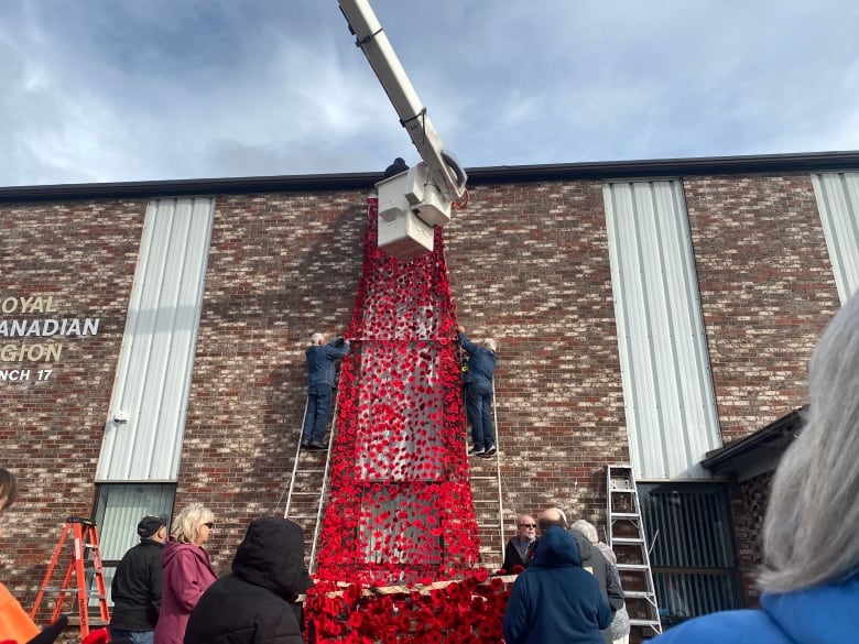 A cascade with thousands of knitted poppes hanging from the side of a building.