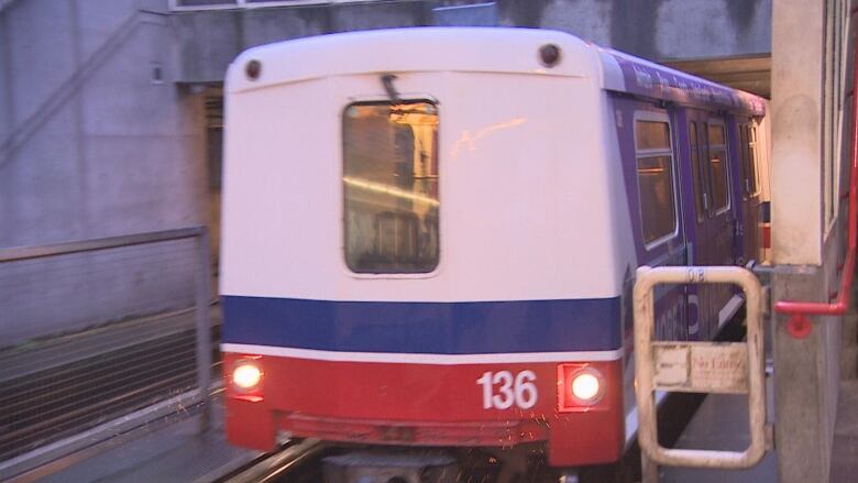 A red, blue and white SkyTrain approaches a platform.