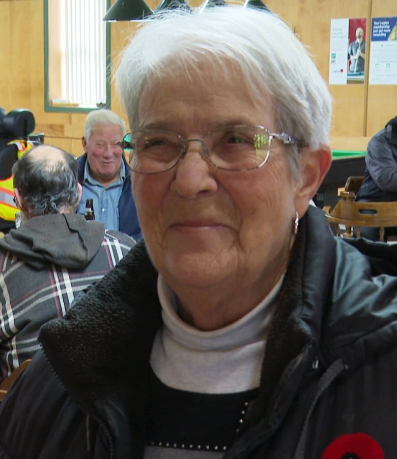 A woman with short white hair standing inside a bar at a Royal Canadian Legion.