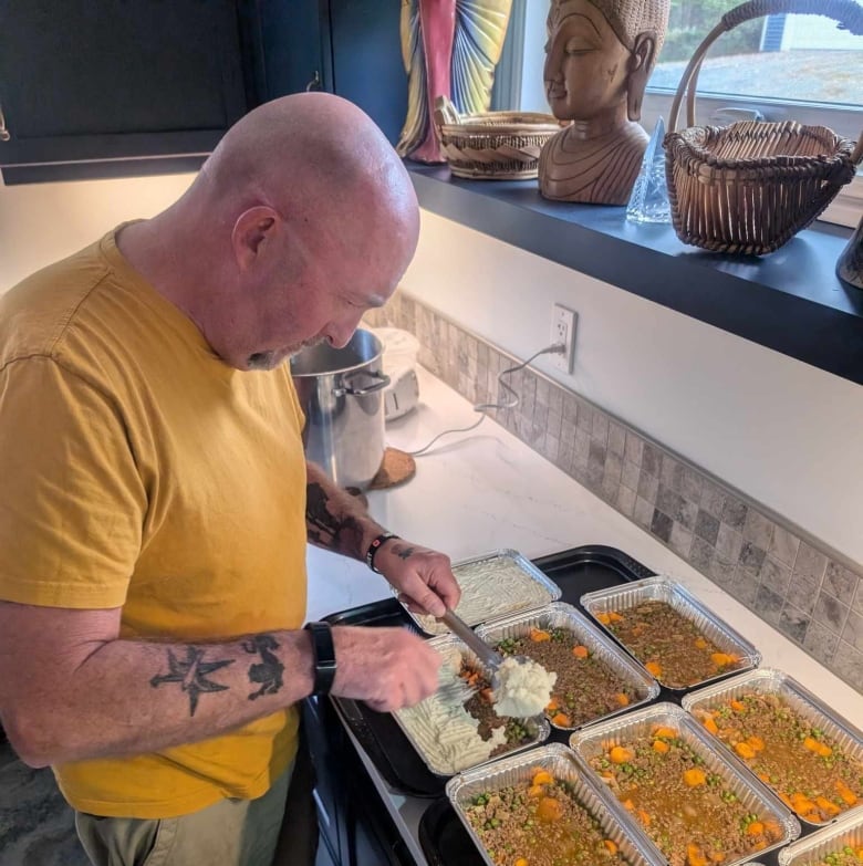 A man puts mashed potatoes on a casserole. 