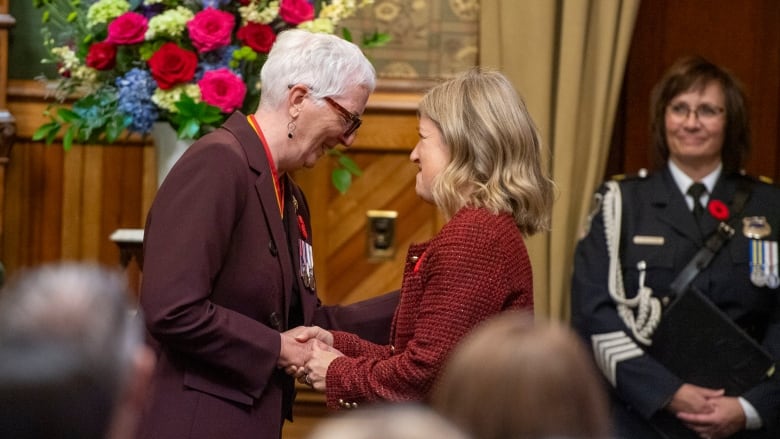 Two women shake hands and smile.