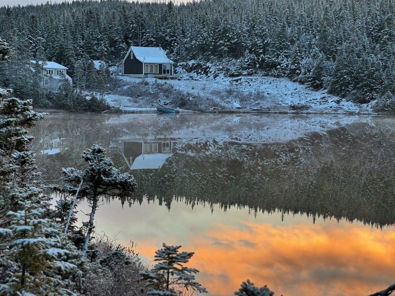 A cabin near a body of water is lightly dusted with snow