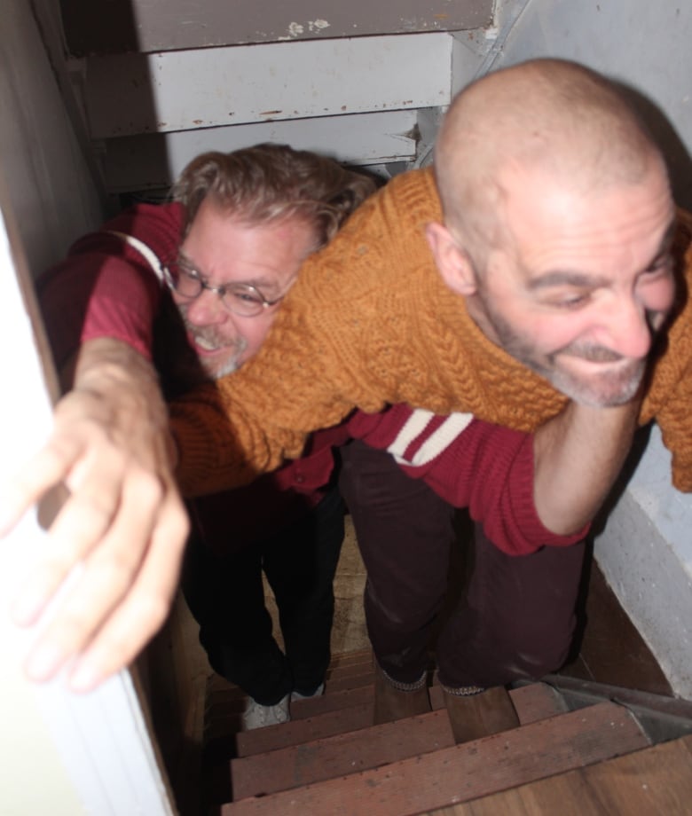 Two men trying to climb up a narrow stairway.