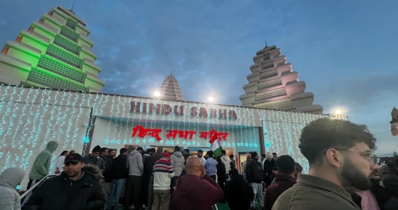 A crowd of people stand outside a Hindu temple on a dark fall evening