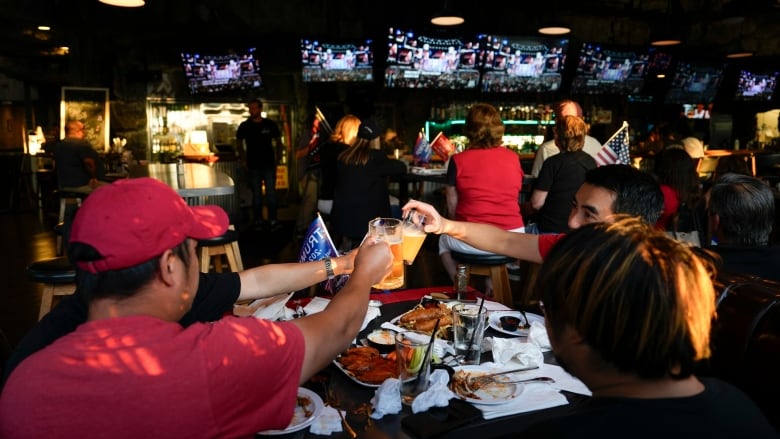 Supporters of former President Donald Trump drink beers as they watch him speak on television on Thursday, July 18, 2024, in Seal Beach, Calif. After knocking on thousands of doors during this year's presidential campaign, David Shelton's work is done  now, he's looking forward to knocking back a drink or two at a local bar on election night with fellow Americans. (AP Photo/Ashley Landis)