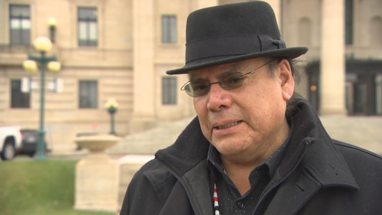 A man in a black hat, sunglasses and clothing speaks.