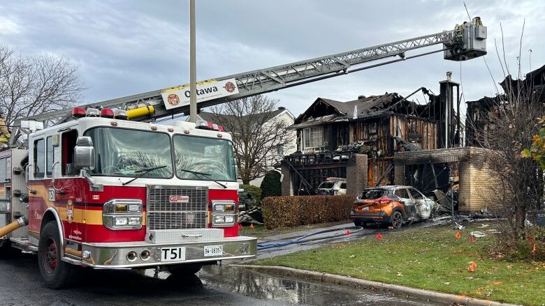 A fire engine parked in front of a burned out residential home with a burned car in the driveway.