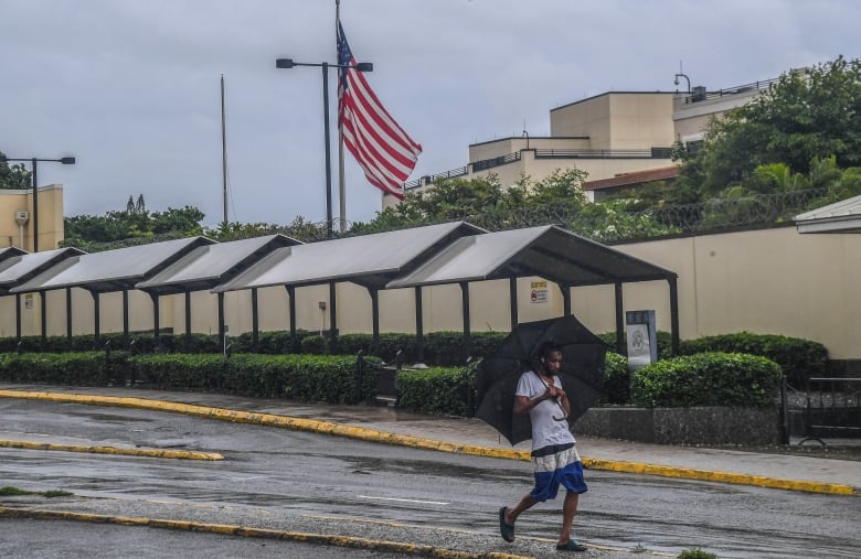 Man walking past the U.S. Embassy in Kingston, Jamaica, during heavy rains brought on by tropical storm Rafael.